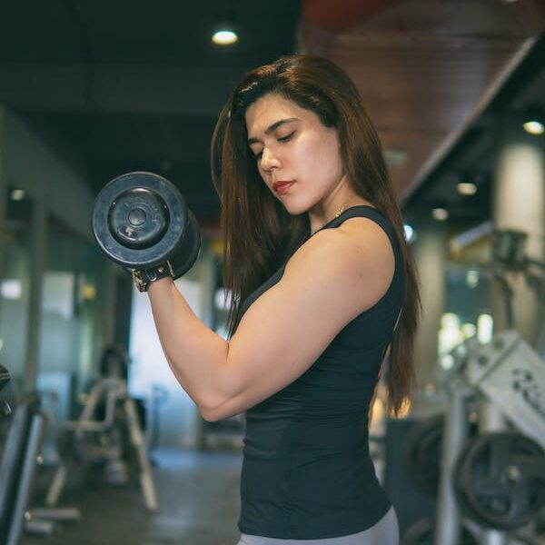 mujer joven haciendo press de biceps con mancuernas